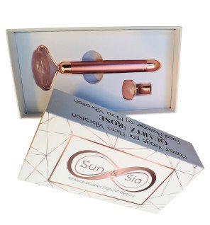 masseur visage électrique en quartz rose posé sur une table en bois clair avec un miroir rond