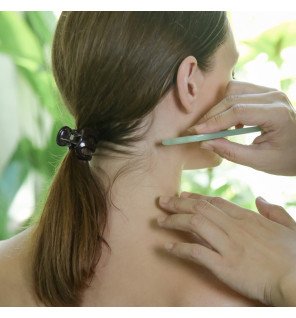 pierre de jade polie pour massage facial posée à côté d’un flacon de sérum