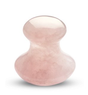 gua sha en quartz rose sur fond neutre mettant en valeur sa couleur délicate