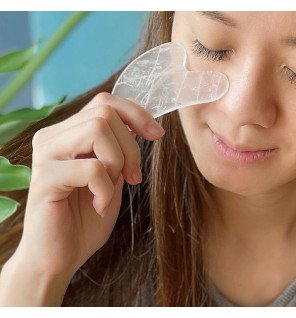 main féminine tenant délicatement le gua sha près du visage