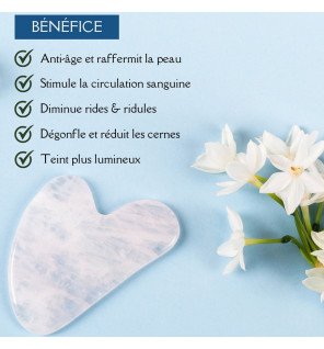 gua sha en cristal de roche placé sur un plateau en bois avec fleurs séchées