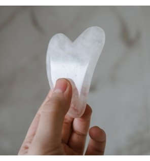 gua sha en cristal de roche à côté d’un flacon d’huile pour le visage