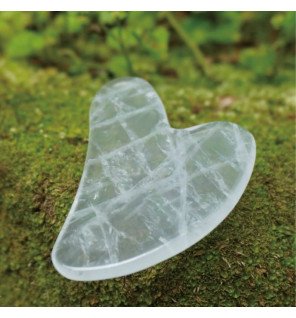 outil de massage gua sha en cristal sur une surface en marbre clair