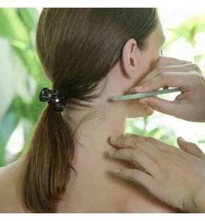 main utilisant la pierre guasha sur la joue pour massage facial