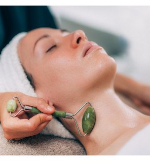 masseur facial en pierre de jade vert utilisé sur une joue pour un massage relaxant